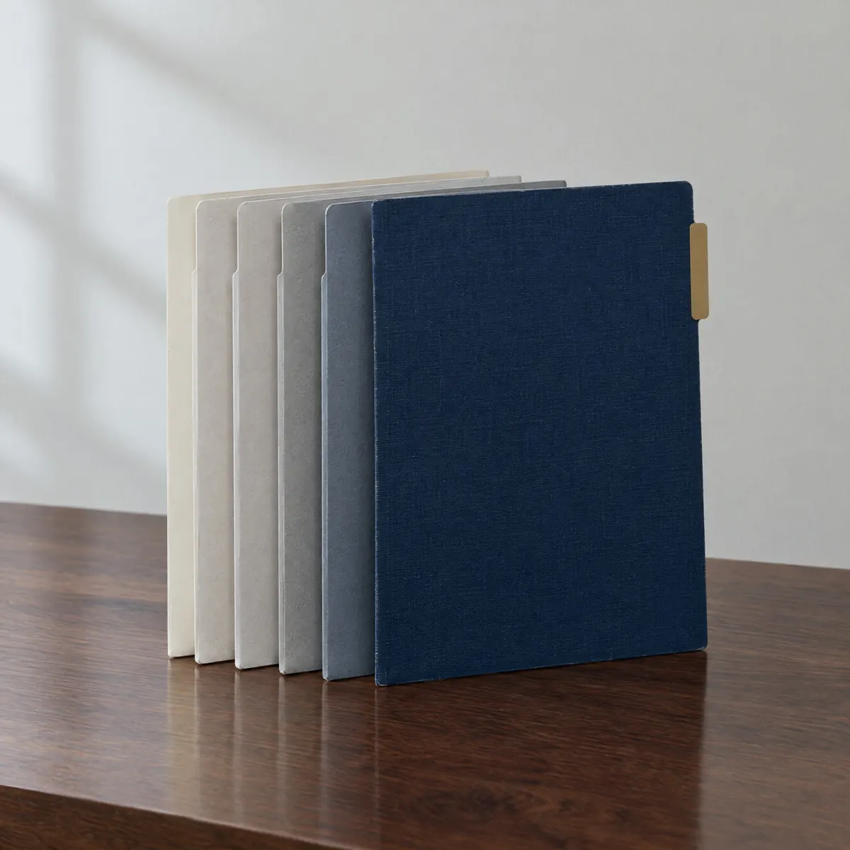 A navy deal folder pulled slightly forward from a row of neutral folders on a table, with one muted gold tab
