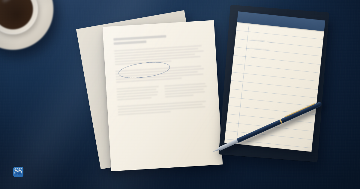 A blurred one-page teaser beside a blank lined notepad and navy pen on a dark worktable